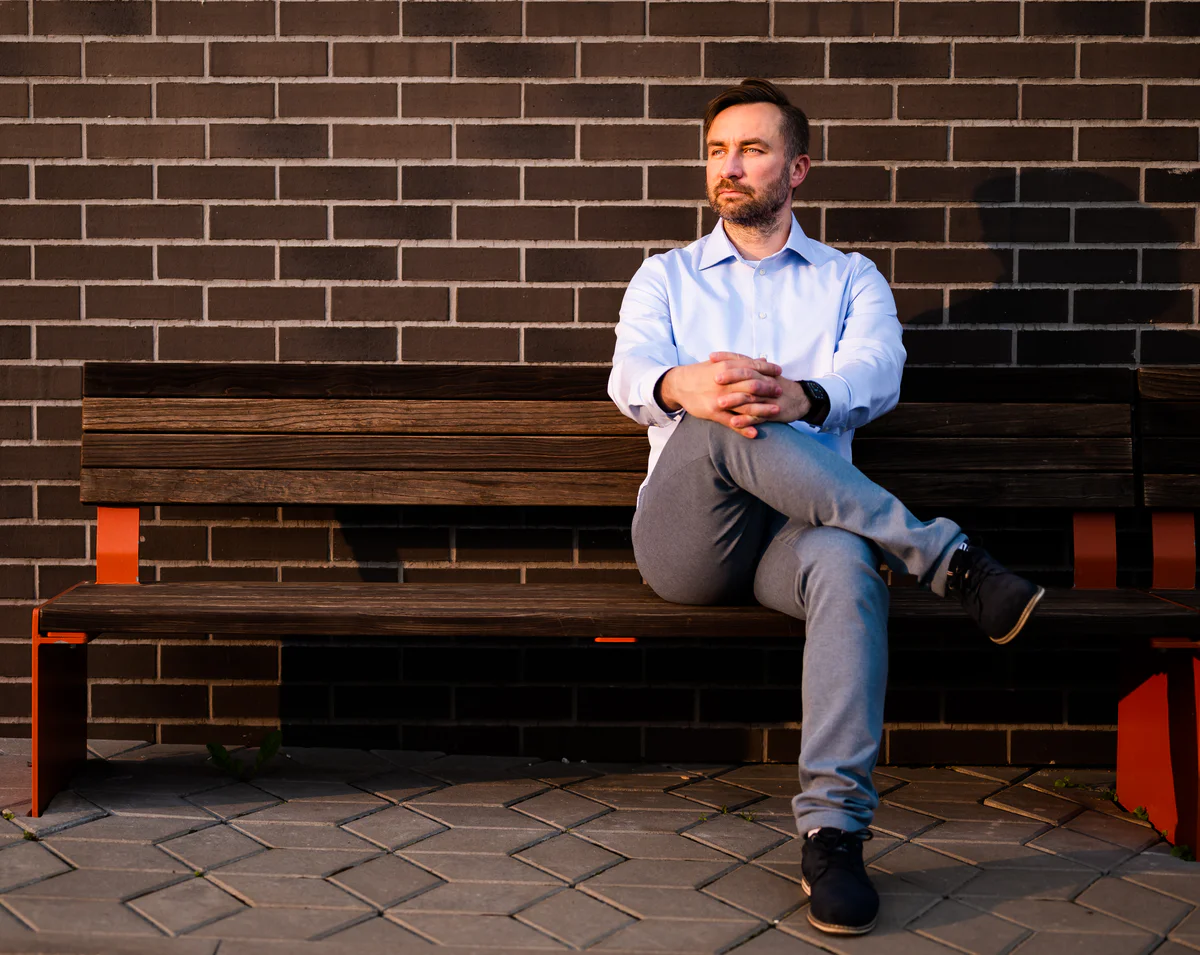 Anti Soosaar sitting on wooden bench by brick wall, formal pose (Anti istub puupingil tellisseina taustal, sirge kehahoiak)
