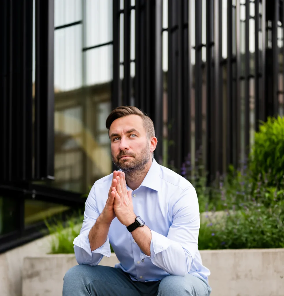 Anti Soosaar sitting outside modern building with folded hands (Anti istub moodsa hoone ees, käed koos, rahulik hoiak)