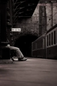 Black and white image of train platform with solitary foot resting on bench (Mustvalge pilt rongijaamast, pingil lebav jalg – ootusmoment)