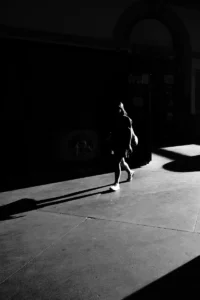 Person walking through side-lit street scene, elongated shadow in black and white (Isik kõnnib tugevas külgvalguses, pikk vari tänaval, mustvalge foto)