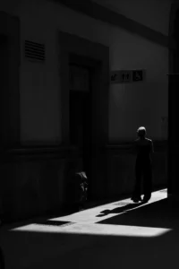 Woman walking in shadows near doorway, strong contrast black and white (Naine liigub ukse lähedal valguse ja varju piiril, mustvalge kontrast)