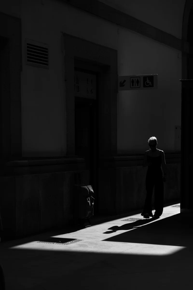 Woman walking in shadows near doorway, strong contrast black and white (Naine liigub ukse lähedal valguse ja varju piiril, mustvalge kontrast)