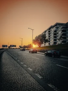 Sunset light over cobblestone street with cars and modern buildings in Porto (Päikeseloojang Portos, munakivitee ja liiklus kaasaegsete hoonete vahel)