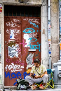 Young man sitting on a city sidewalk in Porto, surrounded by graffiti and cables (Noormees istub Porto tänaval grafitiseinte ja elektrijuhtmete keskel)