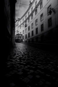 Narrow cobbled street with a tram emerging from shadow in black and white Porto scene (Mustvalge stseen Portost – kivisillutisega tänav ja tramm valgusest välja sõitmas)