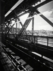 Black and white photo of steel bridge structure with view over Lisbon river (Mustvalge foto Lissaboni terassillast )