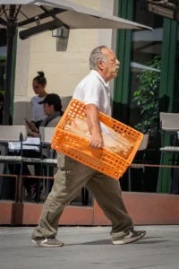 Man carrying an orange crate past outdoor café in Porto (Mees kõnnib oranži kastiga Porto kohviku ees)