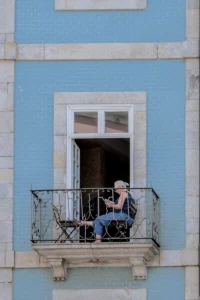 Elderly woman using a laptop on a blue balcony in Porto (Eakas naine rõdul sülearvutiga Porto elumajas)