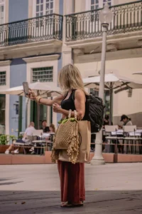 Woman standing in Porto plaza with shopping bag and phone in hand (Naine seisab Porto väljakul, käes nutitelefon ja võrgust ostukott)