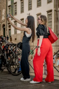 Two women taking a selfie on a raised sidewalk in Porto, with bicycles nearby (Kaks naist teevad selfit Porto linnatänaval jalgrataste kõrval)