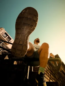 Low angle shot of man sitting with shoe sole in foreground, urban background (Madalvõte mehest istumas, esiplaanil jalatalla detail, taustal linn)