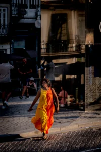 Woman in orange dress walking through sunlit Porto street (Naine oranžis kleidis kõnnib päikesevalguses Porto tänaval)