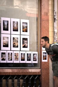 Man closely observing João Cabral photo prints in storefront display in Porto (Mees uurib tähelepanelikult fotoprinte poeakna väljapanekul Portos)