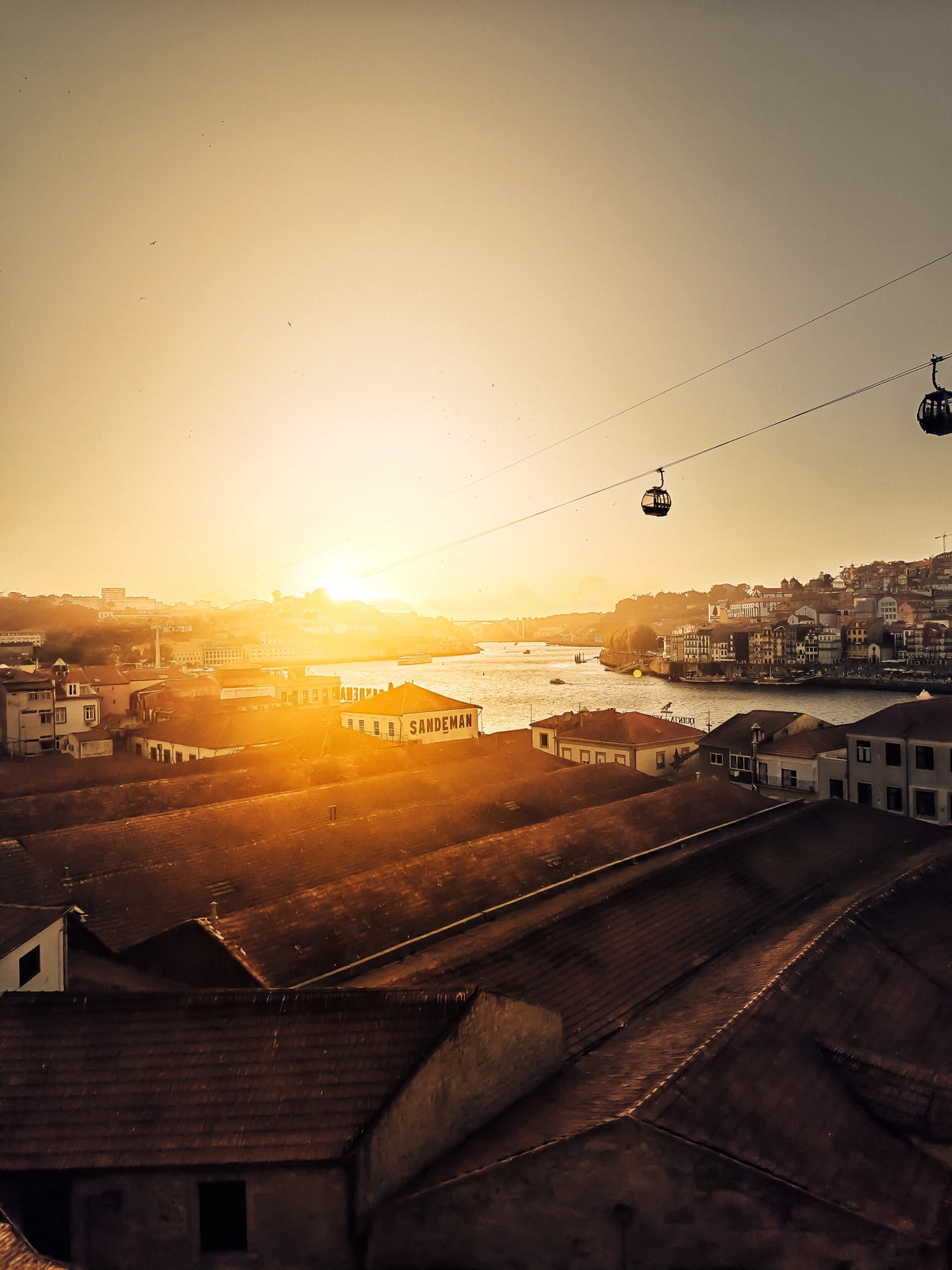 Sunset over Porto rooftops with cable cars floating above the Douro River (Porto tunnetus selgelt äratuntav, soe kuldne valgus, visuaalne rahu)
