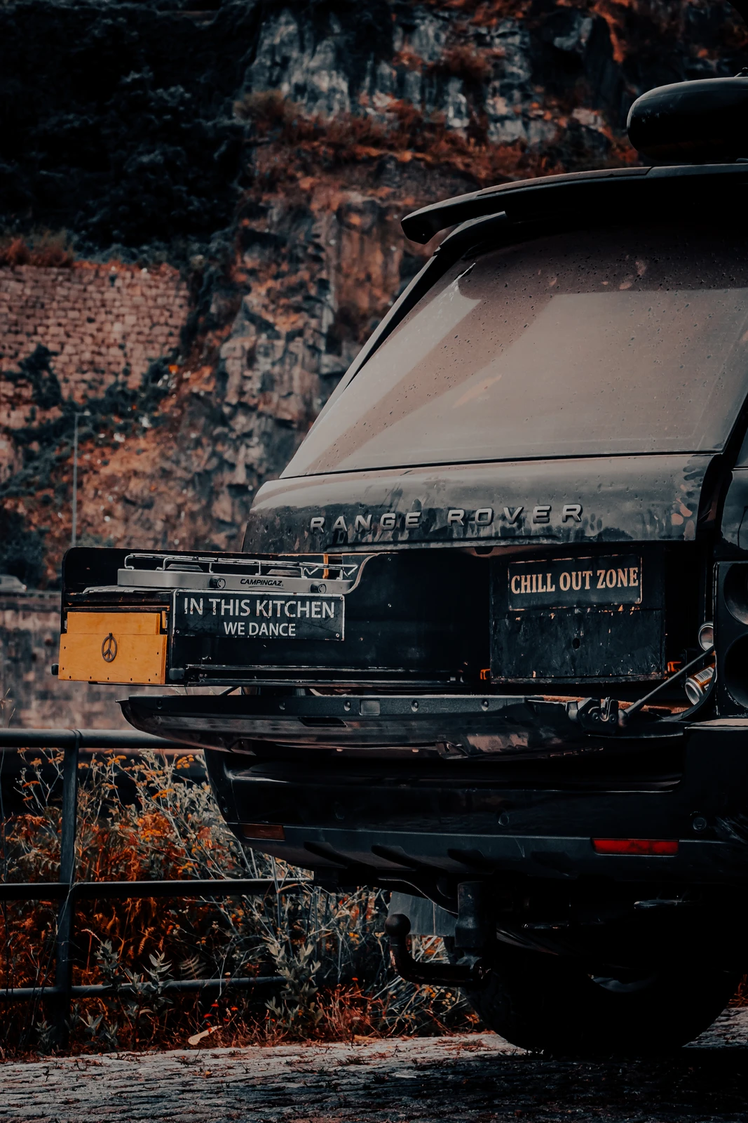 Repurposed black Land Rover turned into a barbecue with humorous kitchen sign (Tugev visuaalne huumor, industriaalne street art vibe)