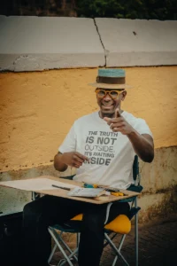 Smiling street artist Gaspar Silva with hat and “Truth is inside” shirt holding pen (Naeratav tänavakunstnik, pliiats käes, tõet-sõnum särgil)