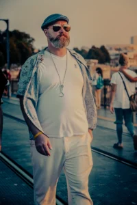 Man in matching white streetwear looking directly at camera in public space (Heledas riietuses mees seisab tänaval ja vaatab otse kaamerasse)