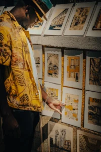 Artist Gaspar Silva in yellow shirt presenting framed ink sketches of buildings (Kunstnik vaatab ülesrivistatud hoonejoonistusi)