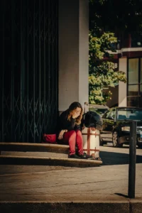 Girl sitting on stairs with head down, light casting hard shadows across frame (Vaikne ja emotsionaalne hetk tänaval)