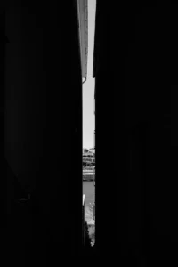 Narrow vertical slice of city street seen between two dark walls (black and white) (Visuaalne kontrast, kitsas perspektiiv linna südames)