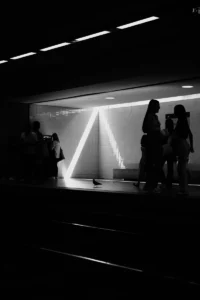 Silhouetted people at metro platform with triangle light installation (Inimeste siluetid metroojaamas kolmnurkse valguskujundiga taustal)