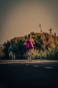 Girl in pink dress cycling uphill under sunset light in nature (Roosas kleidis tüdruk sõidab rattaga loojangutaustal roheluses)