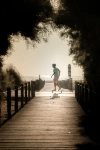 Skater riding longboard through shadowed forest bridge at golden hour (Longboardiga sõitja metsasilla varjus kuldsel tunnil)