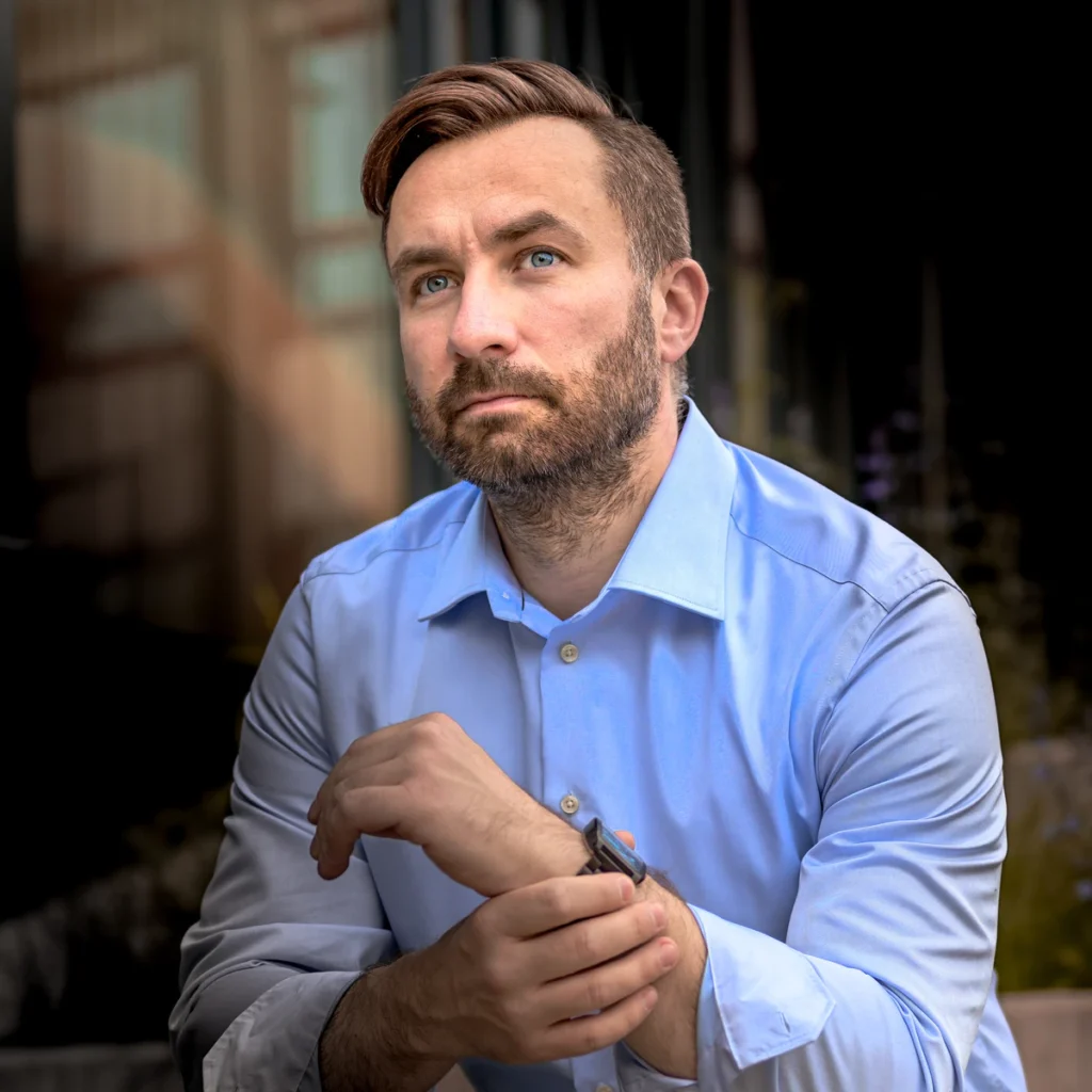 Anti Soosaar sitting outside modern building with folded hands (Anti istub moodsa hoone ees, käed koos, rahulik hoiak)