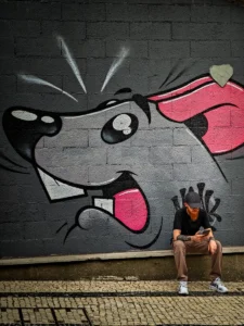 Young man with mask sitting under cartoon rat graffiti in Porto (Noormees maskiga istub graffiti-hiire all Portos)