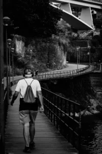 Man walking across narrow bridge near cliff wall in black and white Porto scene (Mees kõnnib kitsal sillal kaljuseina ääres mustvalges Portos)