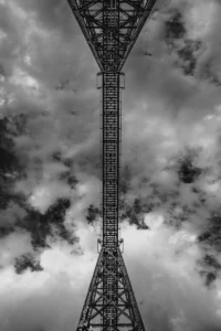 Upward view of tall tower structure in black and white, dramatic sky (Mustvalge vaade üles torni konstruktsioonile, dramaatiline taevas)
