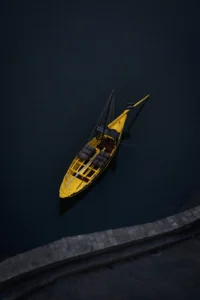 A lone yellow sailboat floating in dark waters, aerial perspective (Graafiline kontrast, minimalistlik tunnetus)