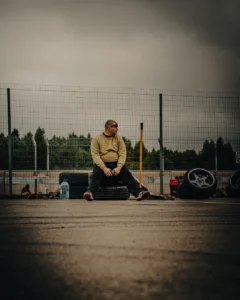 Man in yellow hoodie sitting on asphalt in front of fence with parked cars (Urbanistlik, dokumentaalne) Augustfest