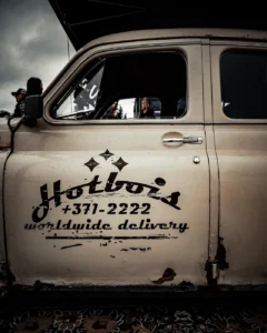 White GAZ with “Hotbois worldwide delivery” text on door at Augustfest 2025 (Street-style visuaal, festivalihuumor)