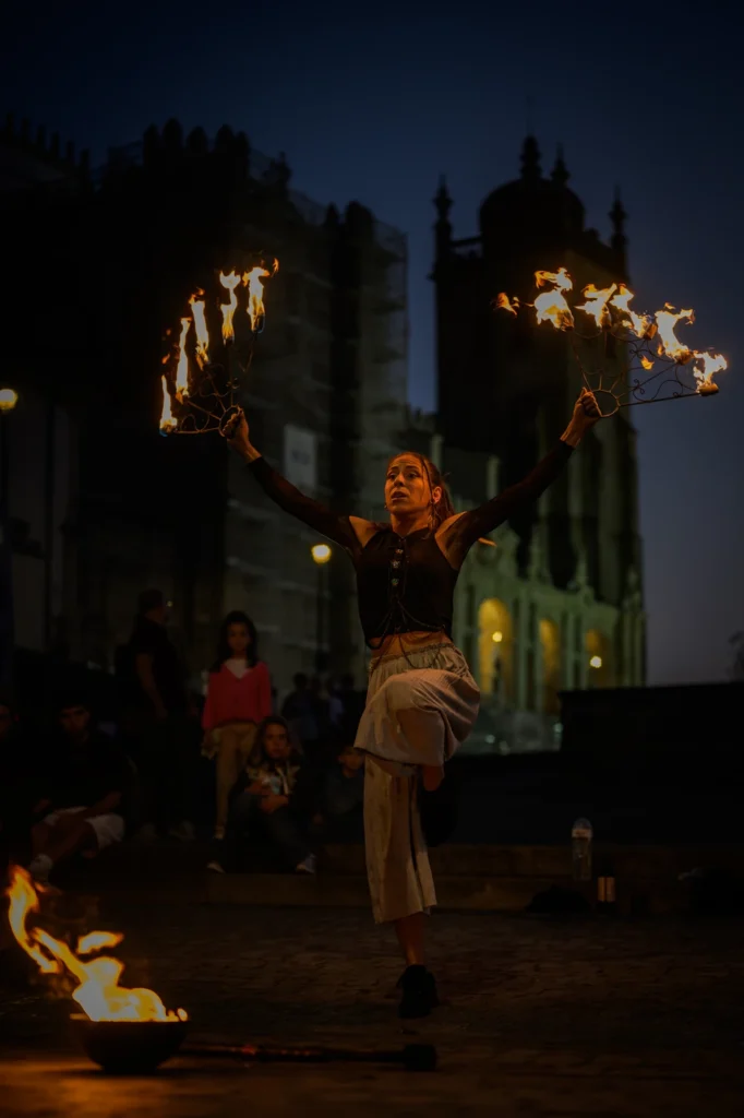 Fire dancer holding glowing flames in hands at dusk performance in Portugal