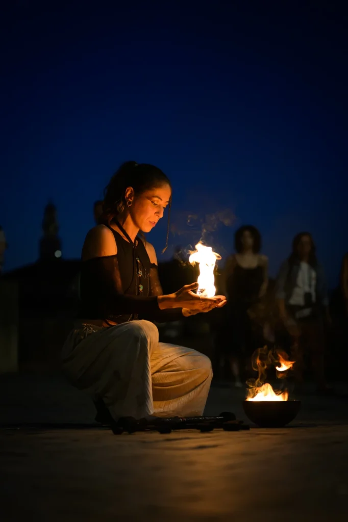 Fire artist kneeling with flames in her hands at dusk, Porto Portugal