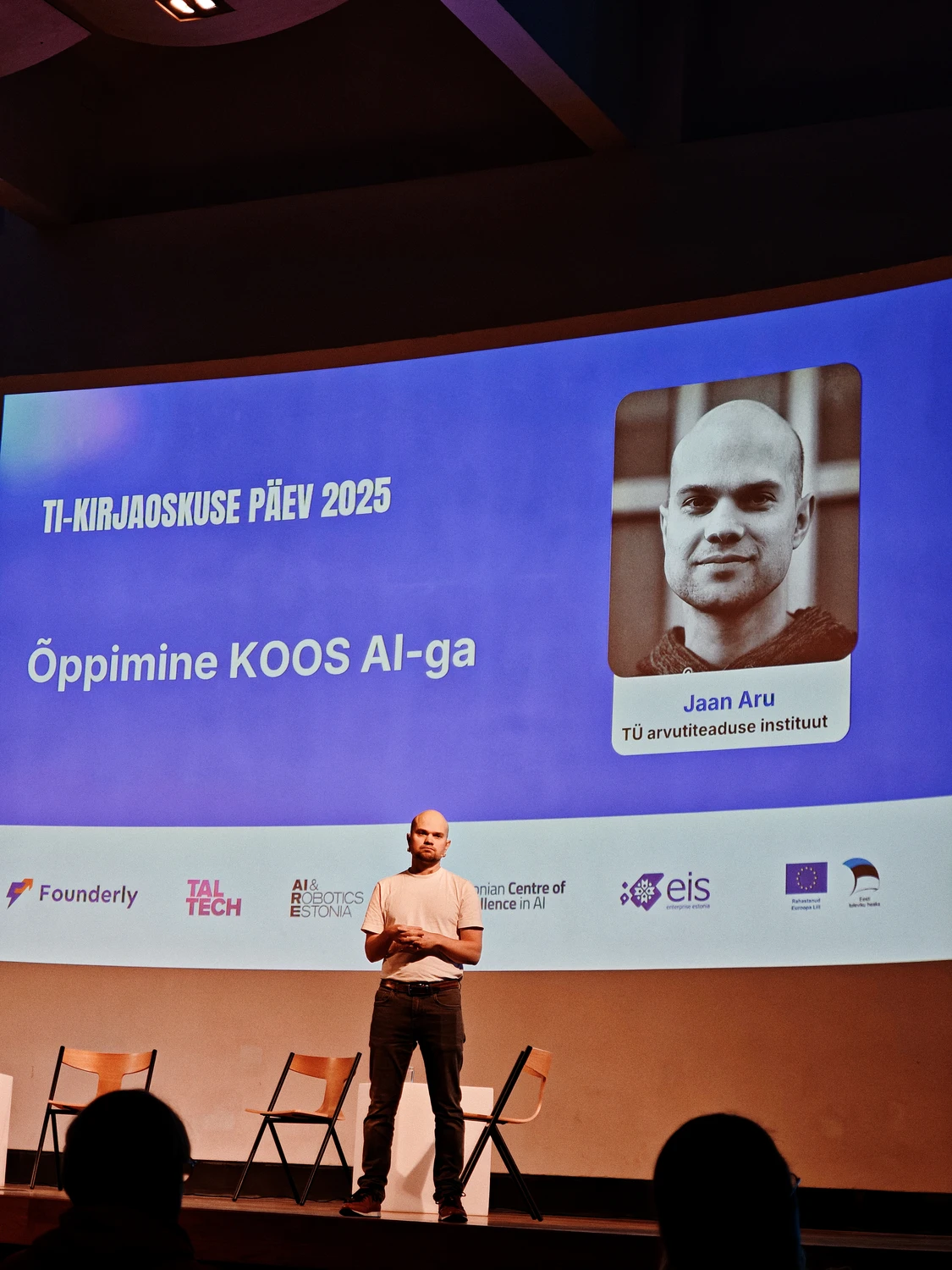 TI-kirjaoskuse päev 2025: kõneleja laval ettekandega „Õppimine koos AI-ga”; sinine ekraan ja partnerite logod taustal. Anti Soosaar