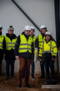 Lähiplaan läikivast nurgakivi kapslist kirjaga "RAND & TUULBERG" ja kahest graveeritud kellust puidust alusel.