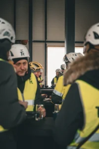 Rivi valgeid Rand & Tuulberg logodega ehituskiivreid ja kollaseid veste puidust kaubaalusel ehitusplatsil.